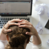 portrait-woman-grabbing-head-desk-near-laptop